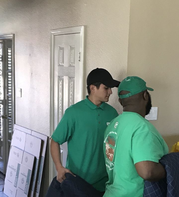 Two Green Van Lines movers carrying moving pads down a hallway past flat-packed boxes