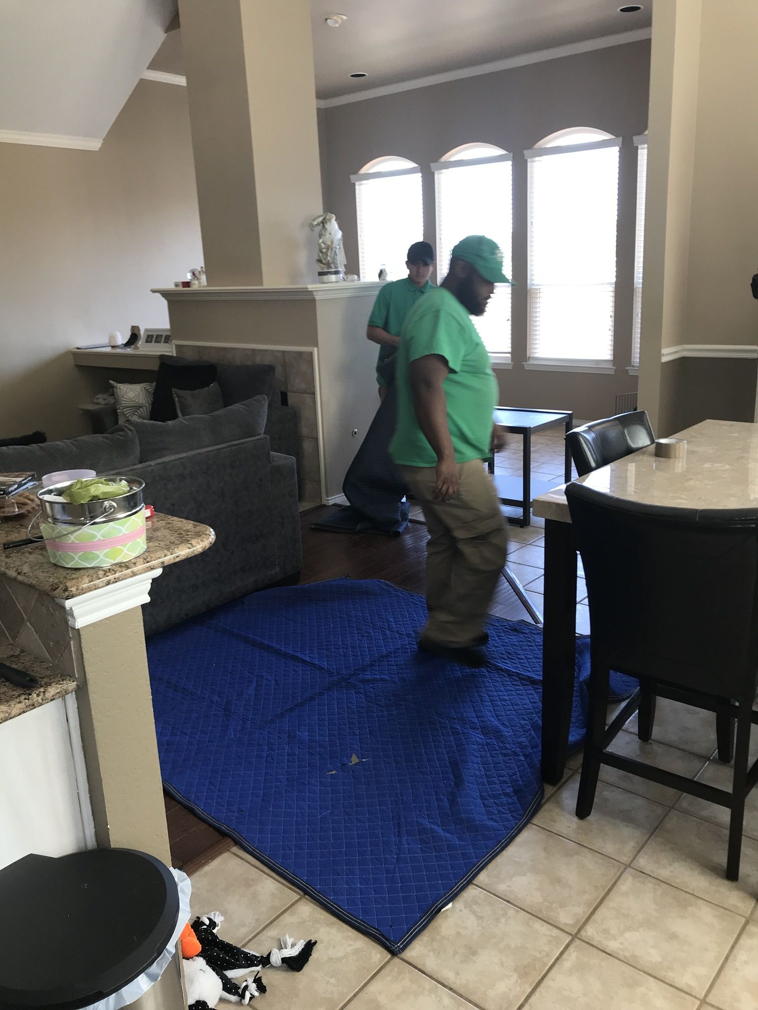 Green Van Lines movers laying moving pads over a hardwood floor inside a customer home