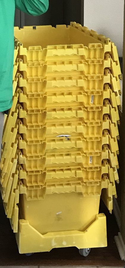 A stack of reusable yellow plastic moving crates on a wheeled dolly